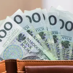 Zasiłek pielęgnacyjny: ile wynosi? Kilka banknotów po 100 zł w brązowym portfelu.