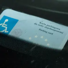 Niebieska karta parkingowa dla osoby niepełnosprawnej z symbolem wózka inwalidzkiego, umieszczona za przednią szybą samochodu.