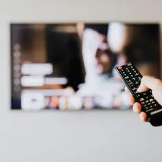 Dłoń trzymająca pilot do telewizora LG na tle wyłączonego ekranu.