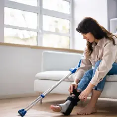 Kobieta z gipsową ortezą na nodze i kulami obok, zastanawia się, zasiłek rehabilitacyjny ile wynosi.