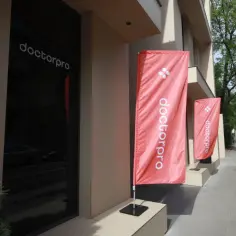 Czerwone flagi z logo "doctorpro" przed nowoczesnym budynkiem kliniki medycznej.