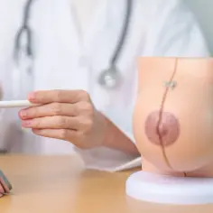 Lekarz z modelem piersi i tabletem, omawiający temat mastektomii.