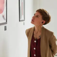 Kobieta w słuchawkach słucha audiodeskrypcji dzieła sztuki w galerii.