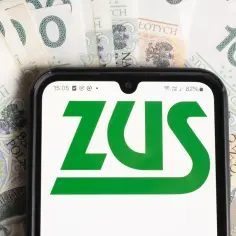 Telefon z logo ZUS na tle banknotów 100 zł. Symbolizuje świadczenia, w tym częściową niezdolność do pracy.