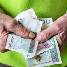 Dłonie trzymają polskie banknoty: 10, 20 i 100 zł. To może być kwota netto renty socjalnej.