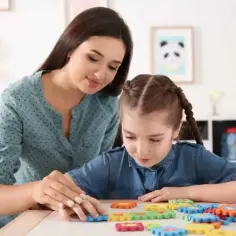 Kobieta pomaga dziecku układać kolorowe puzzle na stole.