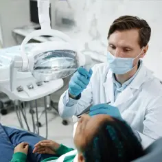Stomatolog w masce i rękawiczkach bada pacjenta w gabinecie dentystycznym.