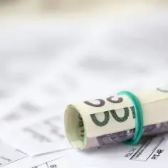 Zwijana sterta banknotów na dokumentach podatkowych. Sprawdź, co można odliczyć w ramach ulgi rehabilitacyjnej.