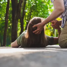 Ktoś doświadcza ataku padaczki na ścieżce w parku, druga osoba próbuje pomóc.