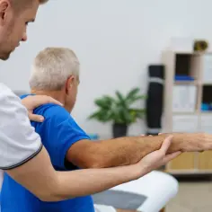 Fizjoterapeuta pomaga starszemu mężczyźnie w ćwiczeniach ramienia.