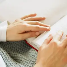 Dłonie czytają książkę w alfabecie Braille'a. To symbol niepełnosprawności, który otwiera świat wiedzy.