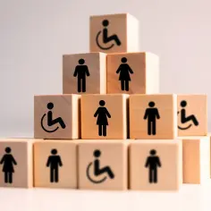 Drewniane klocki tworzą piramidę z symbolami osób, w tym wózka inwalidzkiego, co symbolizuje umiarkowany stopień niepełnosprawności i równość.