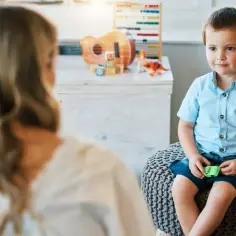 Chłopiec siedzi na pufie, rozmawiając z kobietą. W tle zabawki.