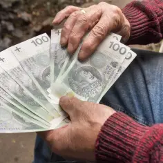 Dłoń trzyma plik banknotów 100 zł. To może być dodatek opiekuńczy dla bliskiej osoby.