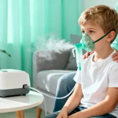 Chłopiec w masce nebulizatora, obok inhalator i ampułki.