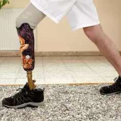 Osoba z protezą nogi w krótkich spodenkach i butach ćwiczy na kamienistym podłożu.