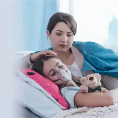 Dziewczynka z maską tlenową, objawy mukowiscydozy. Matka czule głaszcze ją po głowie, obok pluszowy miś.