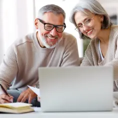 Uśmiechnięta para seniorów z laptopem i notatkami.