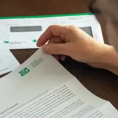 Osoba czyta dokument ZUS, który może być decyzją o przyznaniu emerytury. Widać logo ZUS i fragmenty tekstu.