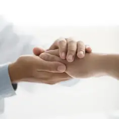Dłoń lekarza w białym kitlu pociesza dłoń pacjenta.