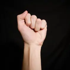 Zaciśnięta pięść z widocznym kciukiem na czarnym tle.