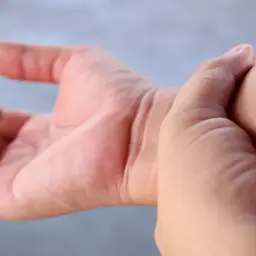 Dłoń uciskana przez inną dłoń, symbolizująca nietypowe objawy fibromialgii, takie jak ból i dyskomfort.