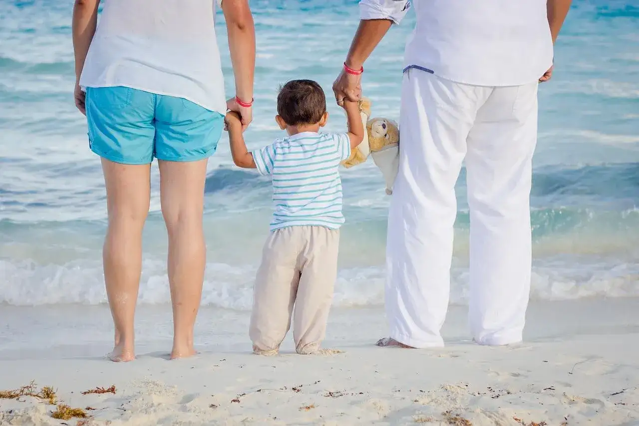 Dziecko trzyma za ręce swoich rodziców, którzy są jego przedstawicielami ustawowymi, na plaży.