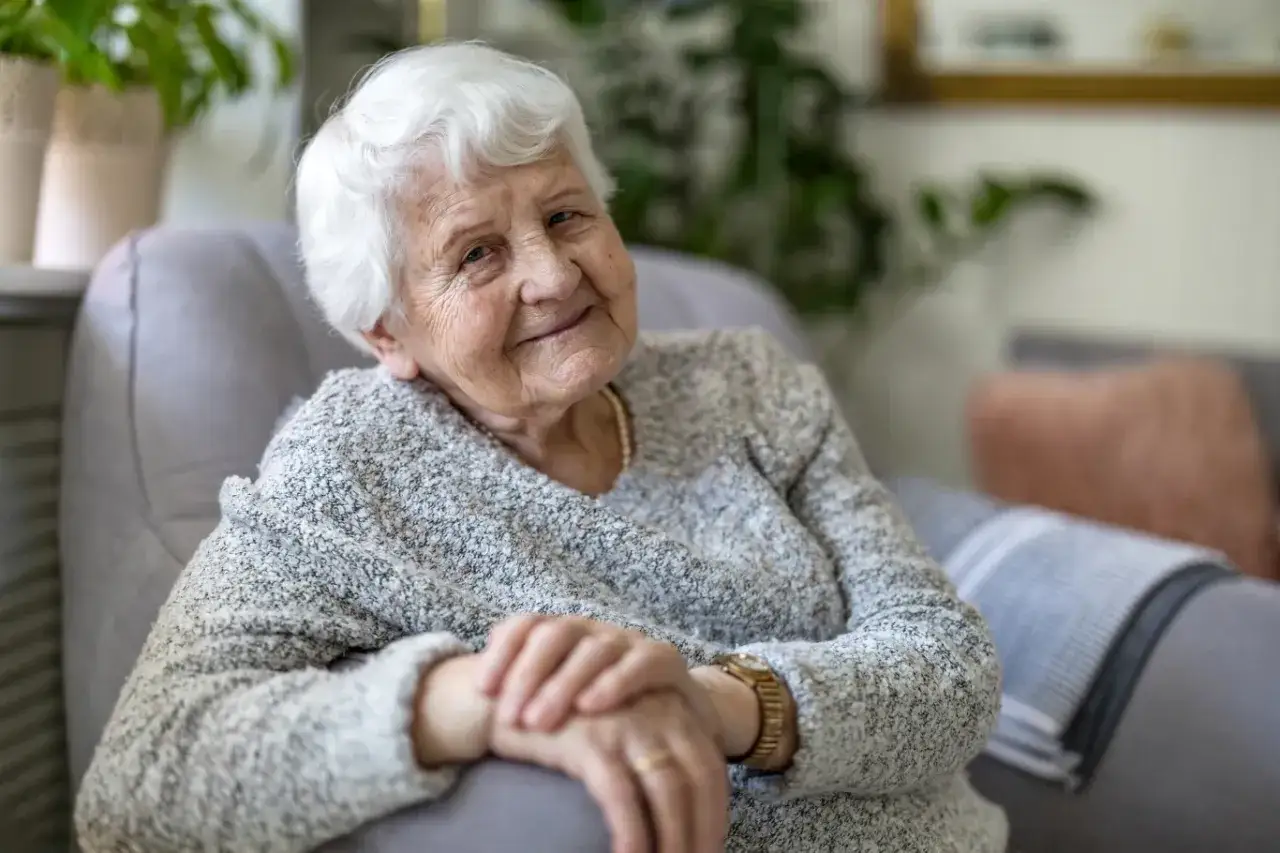 Uśmiechnięta starsza pani z siwymi włosami, siedząca w fotelu. Wsparcie finansowe, jak 500 plus dla chorych na alzheimera, może poprawić komfort życia.